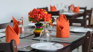 Una mesa de comedor dispuesta con servilletas anaranjadas, copas transparentes y un florero colorido con flores.