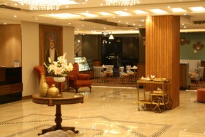 A lobby with a reception desk, a large vase of flowers, a red armchair, and a display cart. - The Secure Inn Hotel (Muscat)