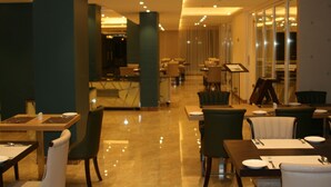 Een modern restaurant met een strak, verzorgd interieur, met een combinatie van eettafels en stoelen, en een heldere, goed verlichte sfeer.
