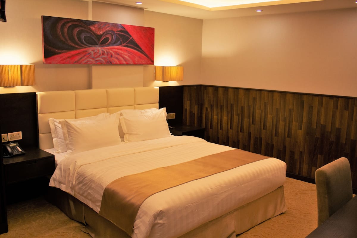 A hotel room with a large bed, two bedside tables with lamps, a wooden accent wall, and a painting above the bed.