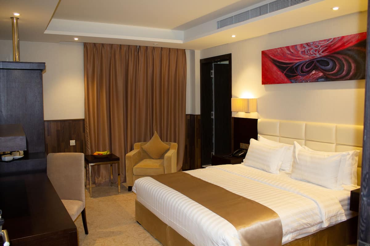 A hotel room with a large bed, a desk, a chair, and a painting on the wall.