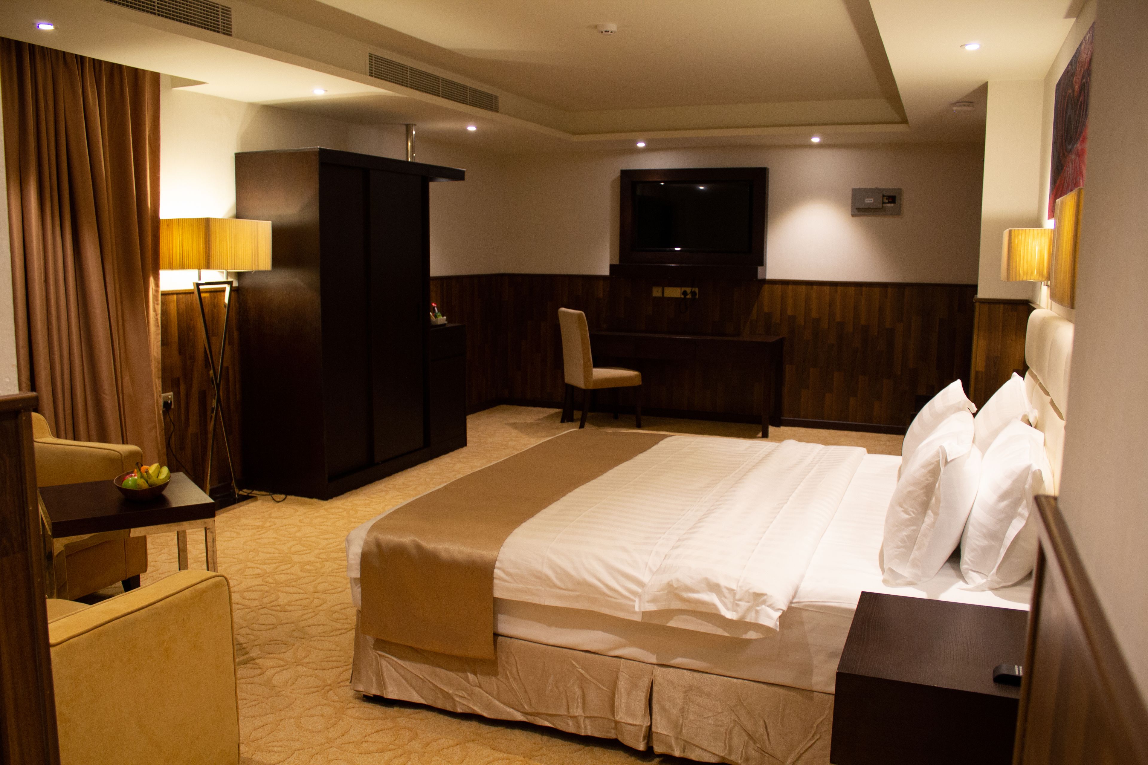 A hotel room with a large bed, a desk, a chair, a television, and a wardrobe.