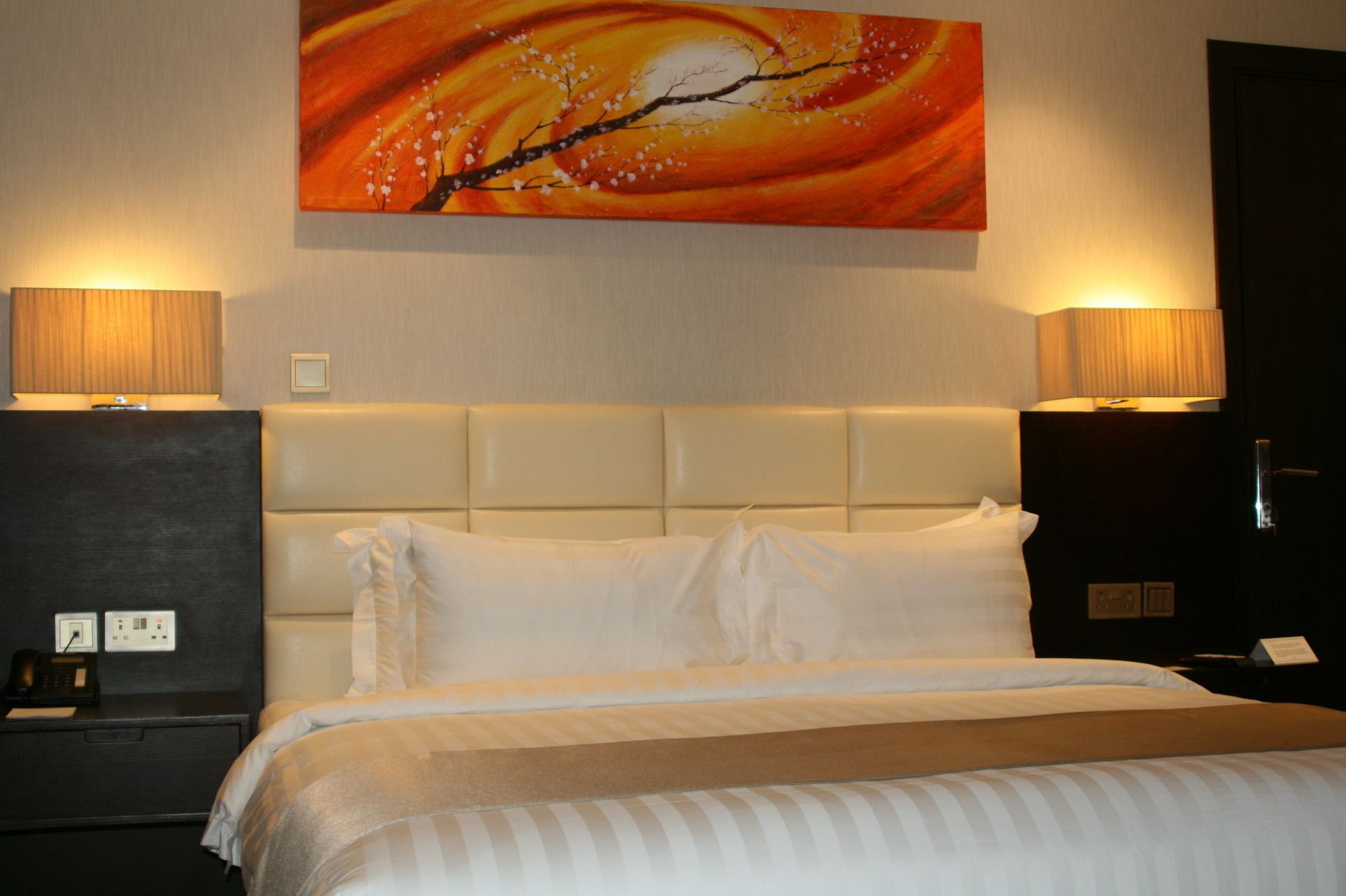 Una camera d'albergo con un letto grande, due abat-jour, un comodino e un quadro appeso al muro.