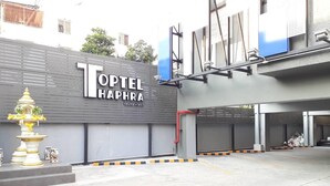 The exterior of Topel Haphra hotel with a modern facade, a large entrance gate, and a decorative fountain. - Toptel Thaphra (Bangkok)