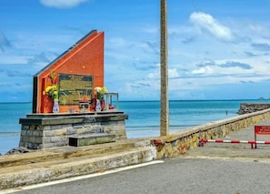 A coastal memorial with a stone structure, a plaque, and flowers.