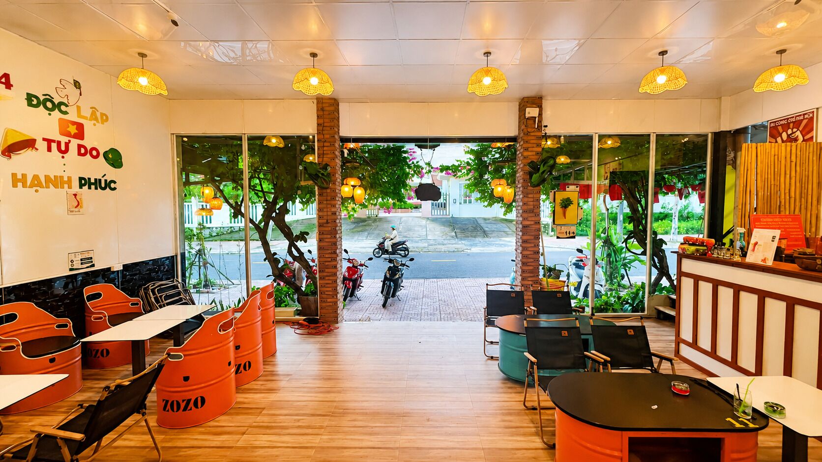 A restaurant interior with wooden flooring, orange seating, and a view of the street outside.