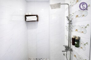 Un baño moderno con paredes de mármol blanco, ducha con cabezal de ducha manual y estante con artículos de tocador.