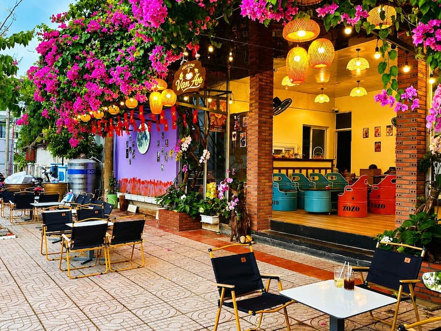 An outdoor café with tables and chairs, a purple wall with decorations, and hanging flowers.