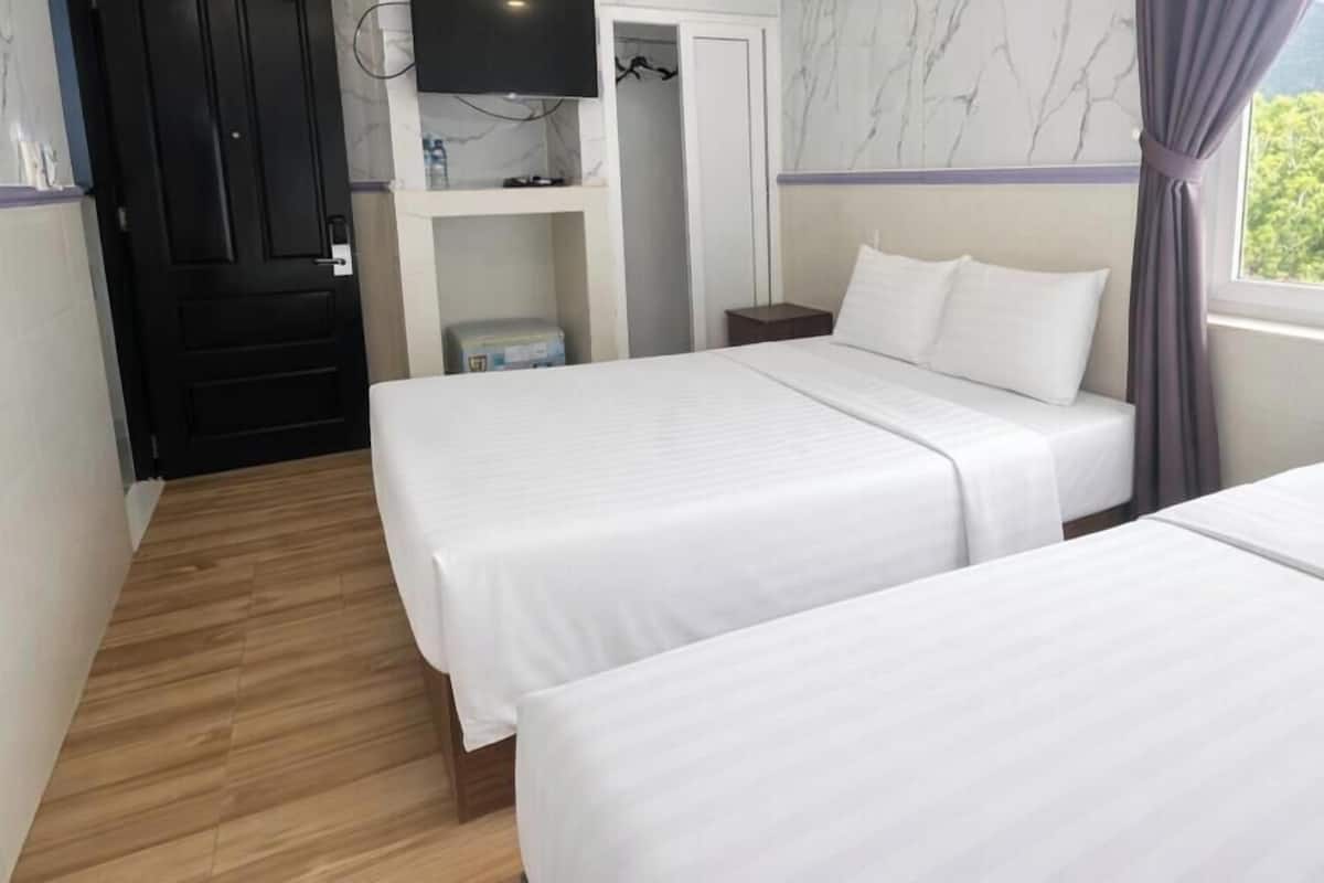 A hotel room with two beds, a wooden floor, a TV on a shelf, and a wardrobe.