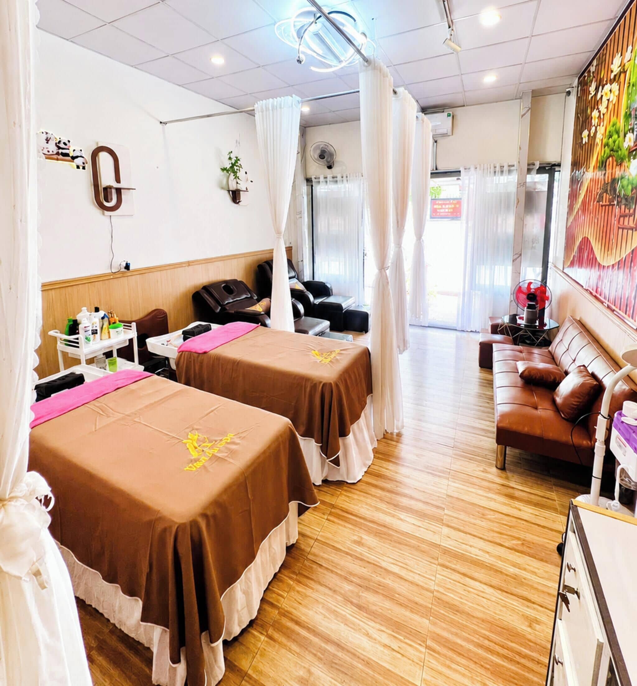 A hotel room with two beds, a sofa, a massage chair, and a small table with toiletries.