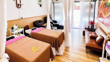 A hotel room with two beds, a sofa, a massage chair, and a small table with toiletries.
