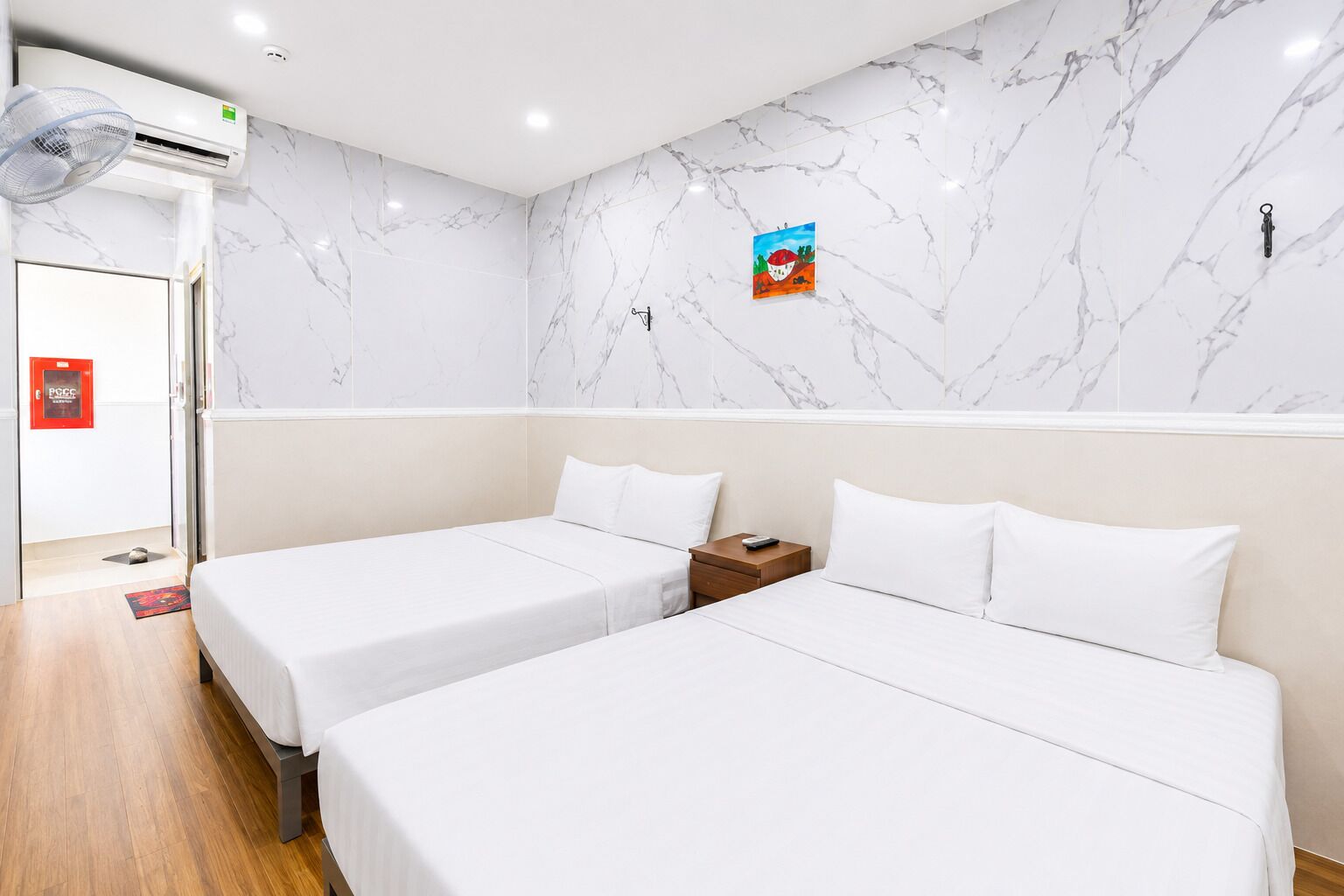 Een hotelkamer met twee bedden, een marmeren wand, een klein schilderij en een rood brandveiligheidsteken.