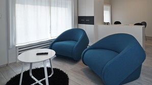 A modern room with two blue armchairs, a small white table, and a kitchenette in the background. - Design Studios SVI-MI (Zagreb)