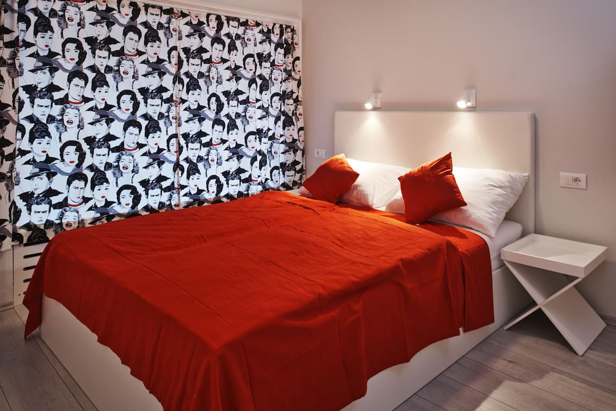A modern bedroom with a red bedspread, white pillows, and a headboard with integrated lighting.