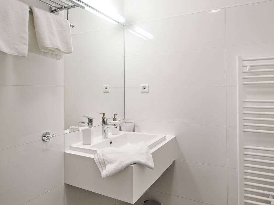 Un baño moderno con lavamanos blanco, espejo y perchero.