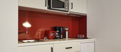 Cocina compacta con armarios blancos, microondas, cafetera y lavavajillas.
