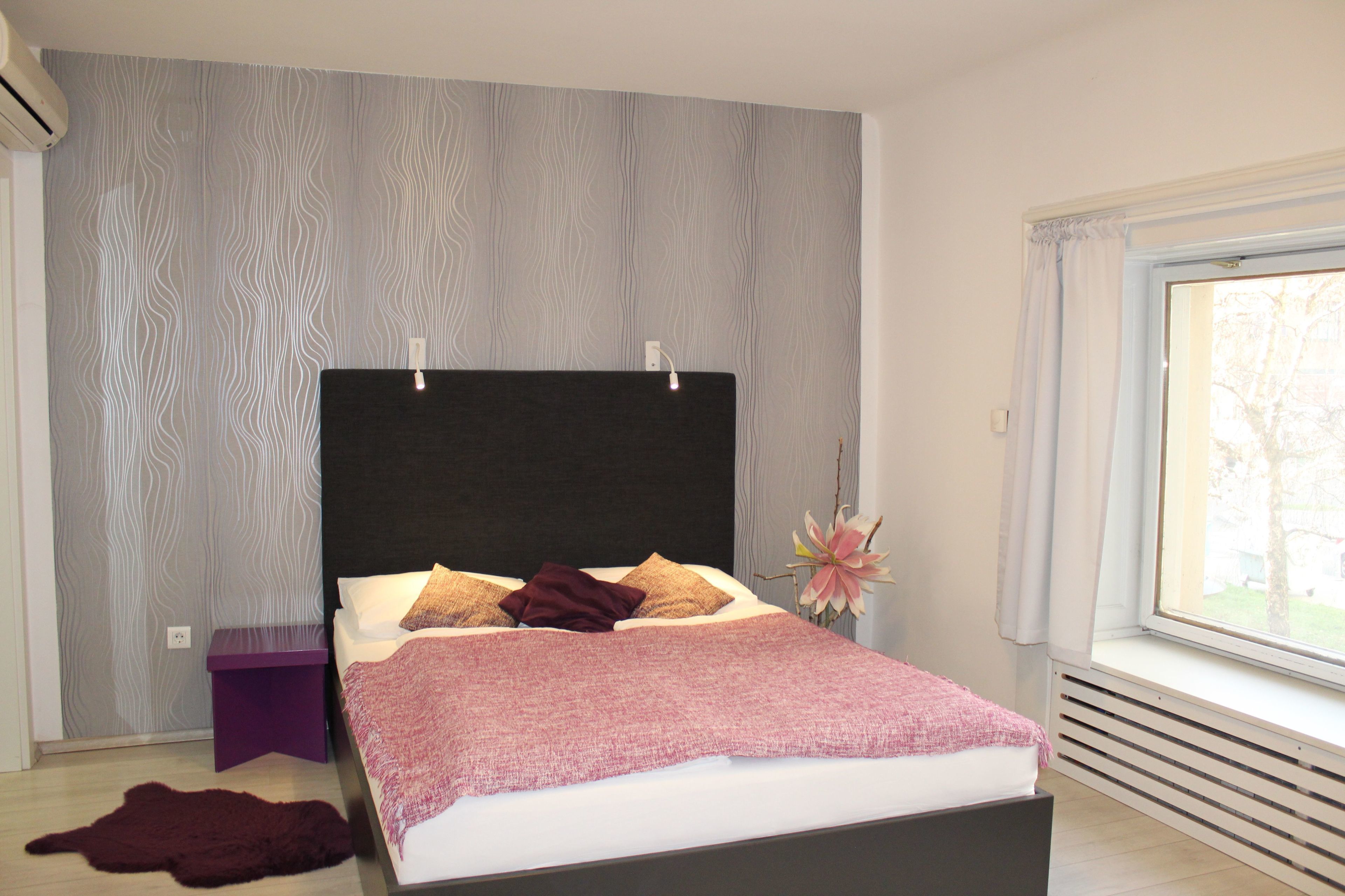 Un dormitorio moderno con una cama grande, una mesita de noche, un jarrón decorativo y vistas a través de una ventana.