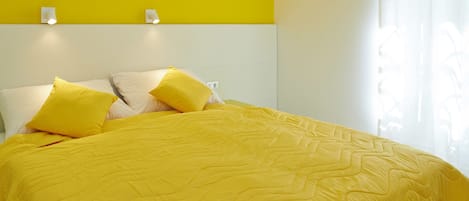 A bed with a yellow quilt and pillows, a white headboard, and a yellow accent wall.