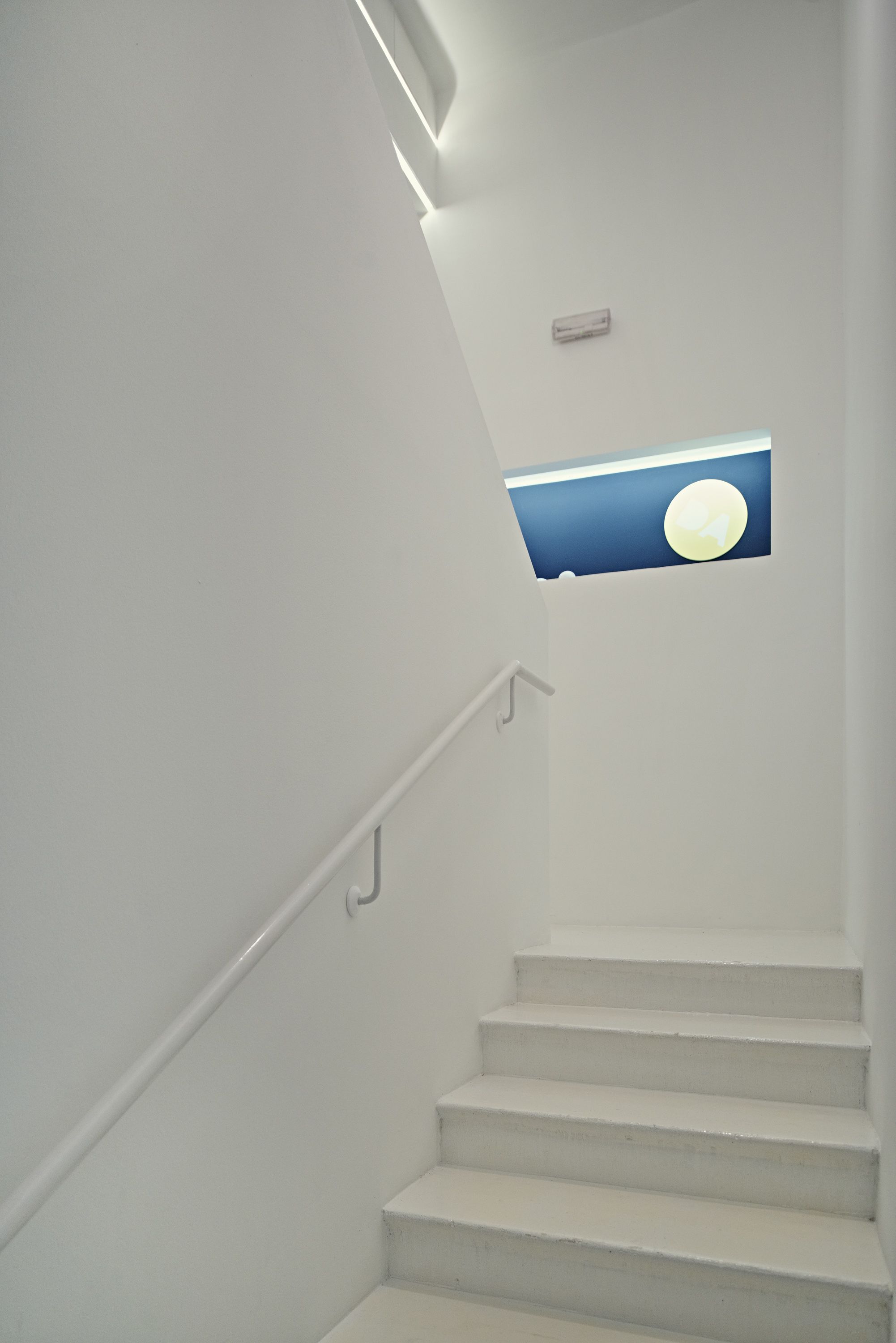 A staircase with white walls and a blue illuminated window at the top.