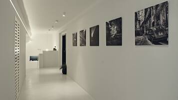 A hallway with a reception desk, a potted plant, and a series of black and white photographs on the wall.