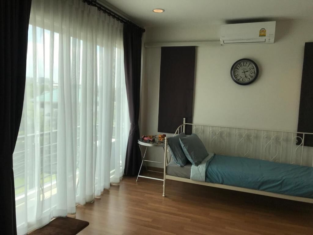 A bedroom with a bed, a bedside table, a clock, and a window with curtains.