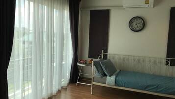 A bedroom with a bed, a bedside table, a clock, and a window with curtains.