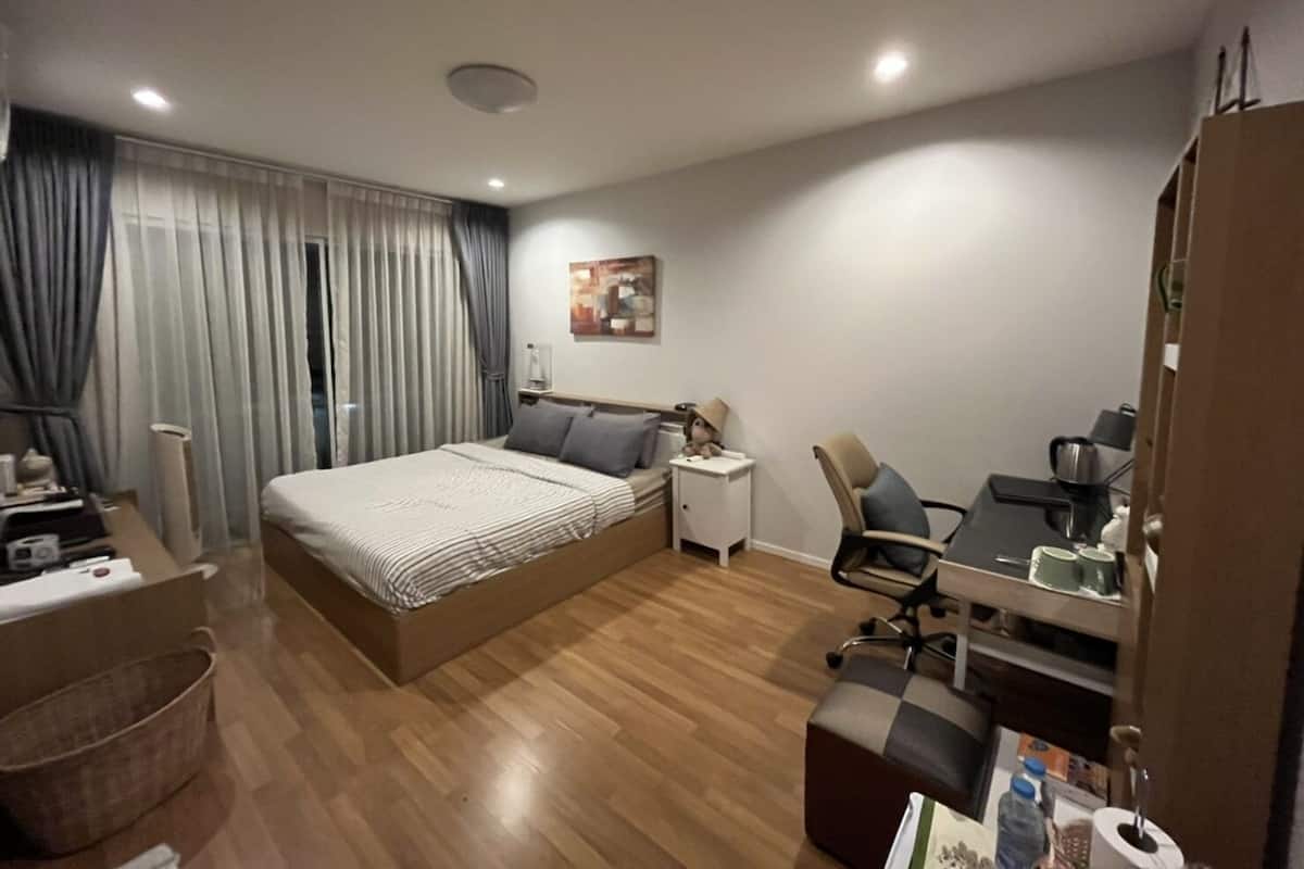A modern hotel room with a large bed, a desk with a chair, a small table, and a wardrobe.