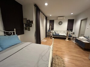 A bedroom with a bed, a bedside table, a small desk with a chair, a window with curtains, and a wall-mounted clock. - Autta House (Bangkok)