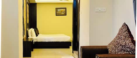 A hotel room with a bed, a sofa, a glass coffee table, and a ceiling fan.