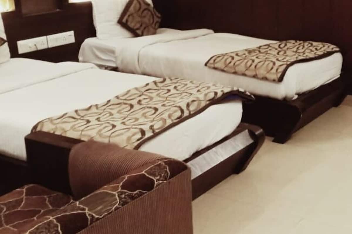 Habitación de hotel con dos camas, un sofá, un cabecero de madera y una mesita de madera.