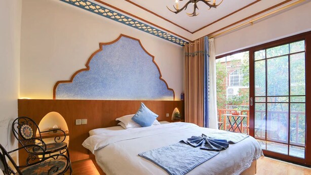 A hotel room with a large bed, a chandelier, a window with a view of greenery, and a decorative wall panel. - Edinburgh Hostel (Zhangjiajie)