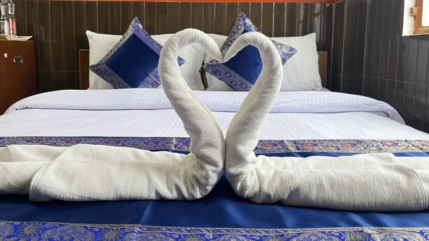 A hotel room with a bed, pillows, and a decorative towel arrangement. - Family Guest House (Varanasi)