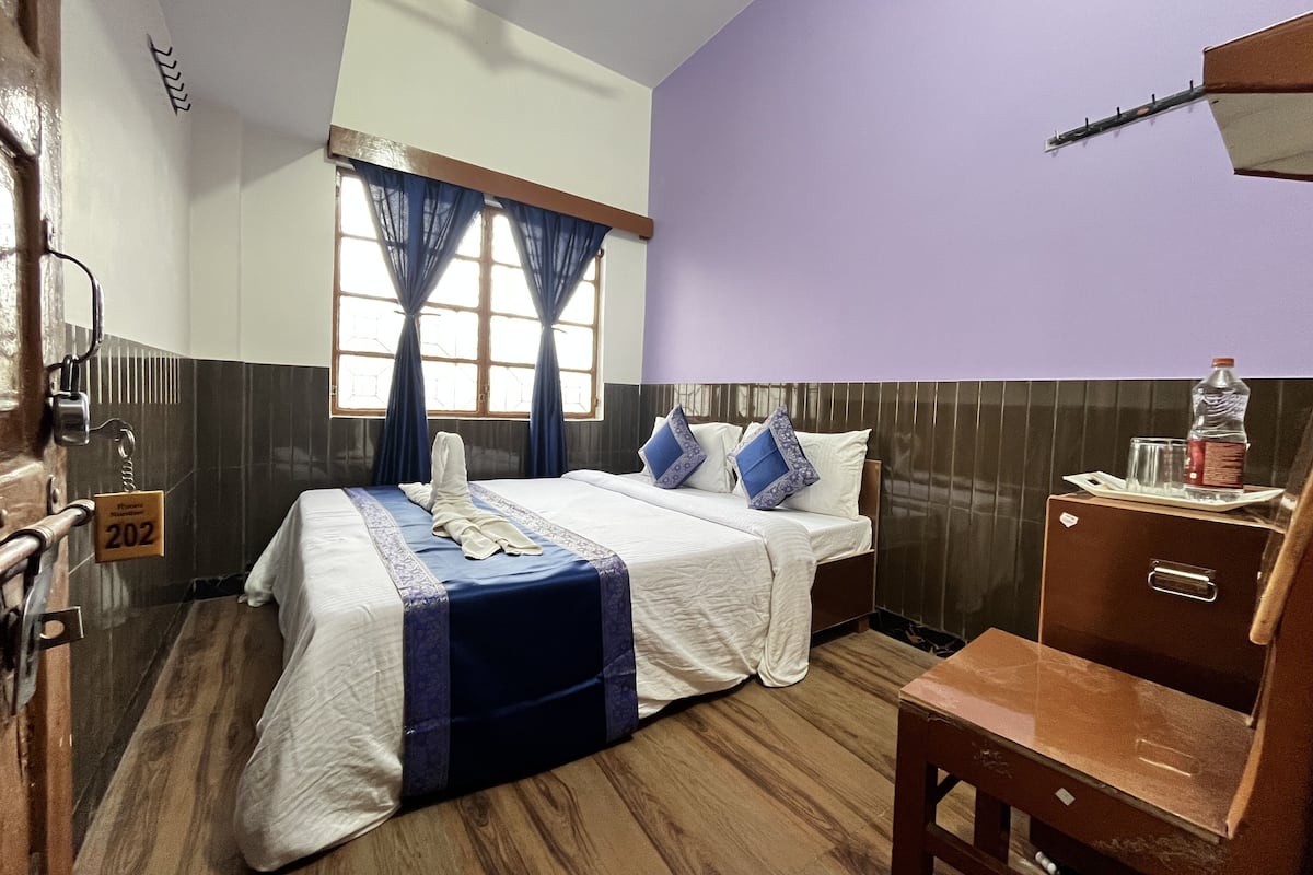 A hotel room with a bed, a desk, a chair, a window with curtains, and a door with a keycard lock.