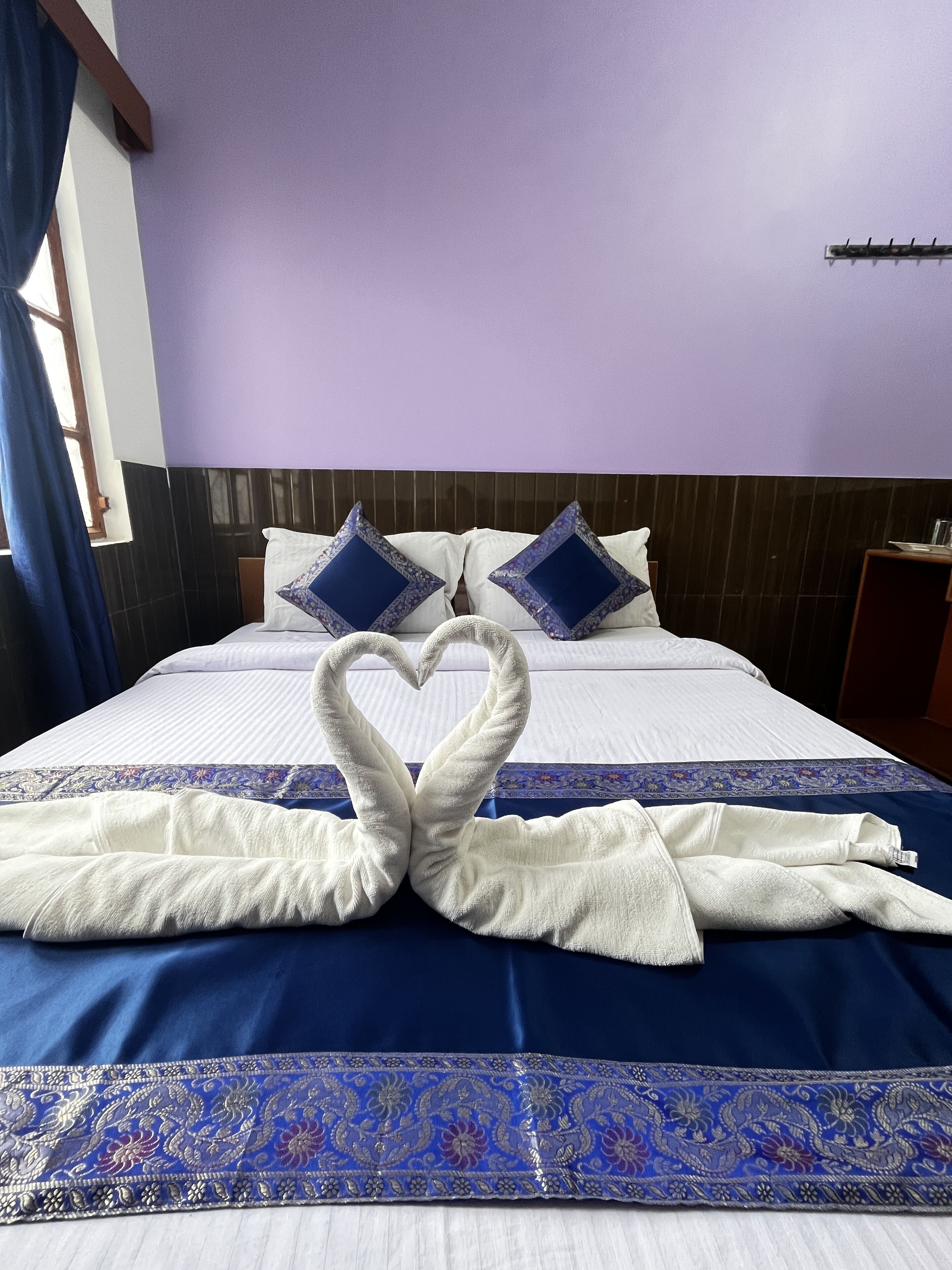 Una habitación de hotel con una cama, dos almohadas y una colcha azul y blanca con un borde decorativo.