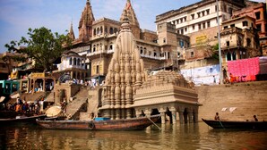 A riverside temple complex with multiple spires and a large central structure, surrounded by traditional buildings and boats on the water. - Family Guest House (Varanasi)