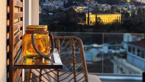 Un balcone con mobili in vimini, un barattolo di vetro e vista sulla città al tramonto.