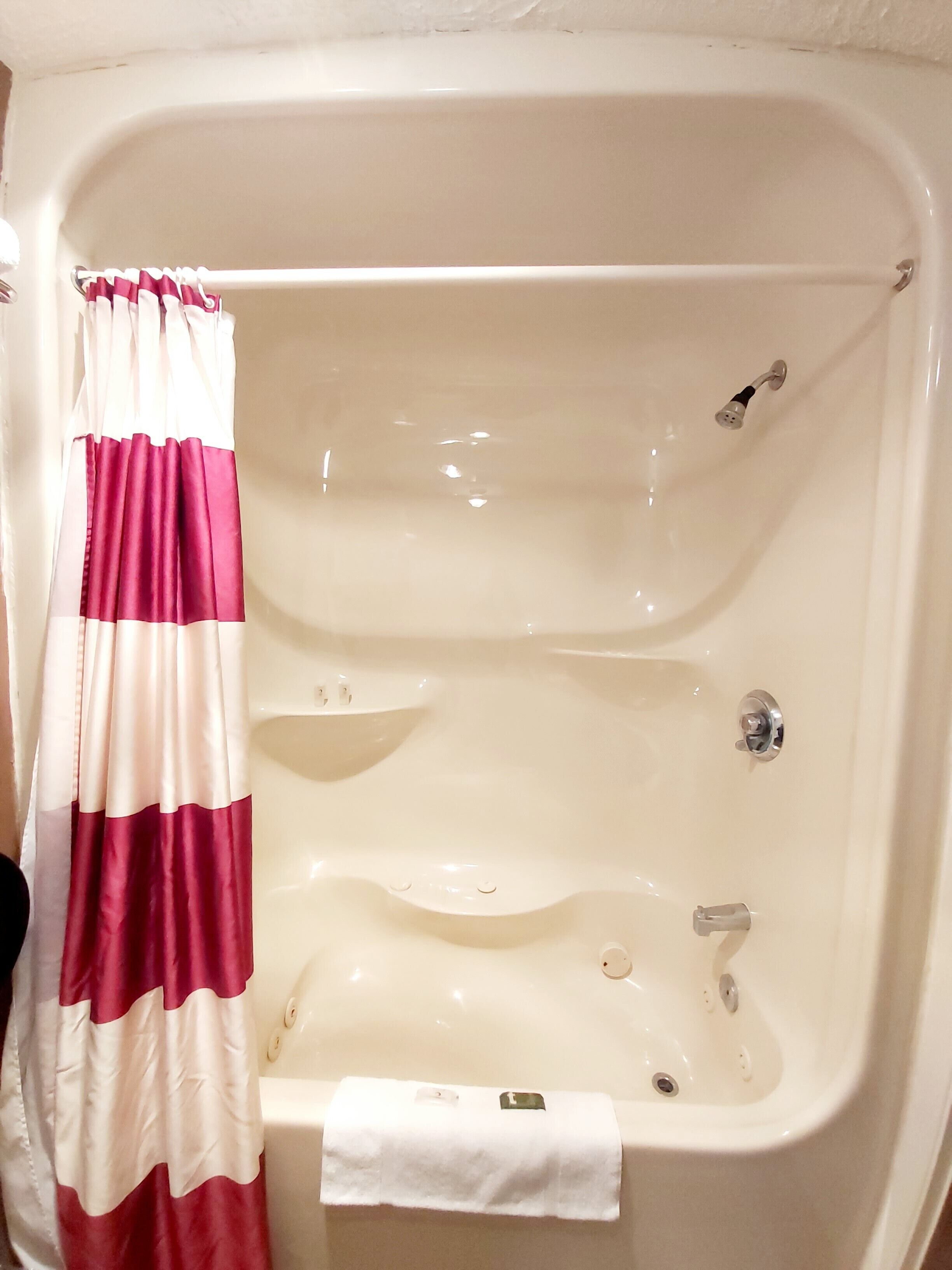 A bathtub with a white and red striped shower curtain, a white towel, and a chrome faucet.
