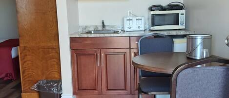 A compact kitchen with wooden cabinets, a microwave, a toaster, and a small dining table with a chair.