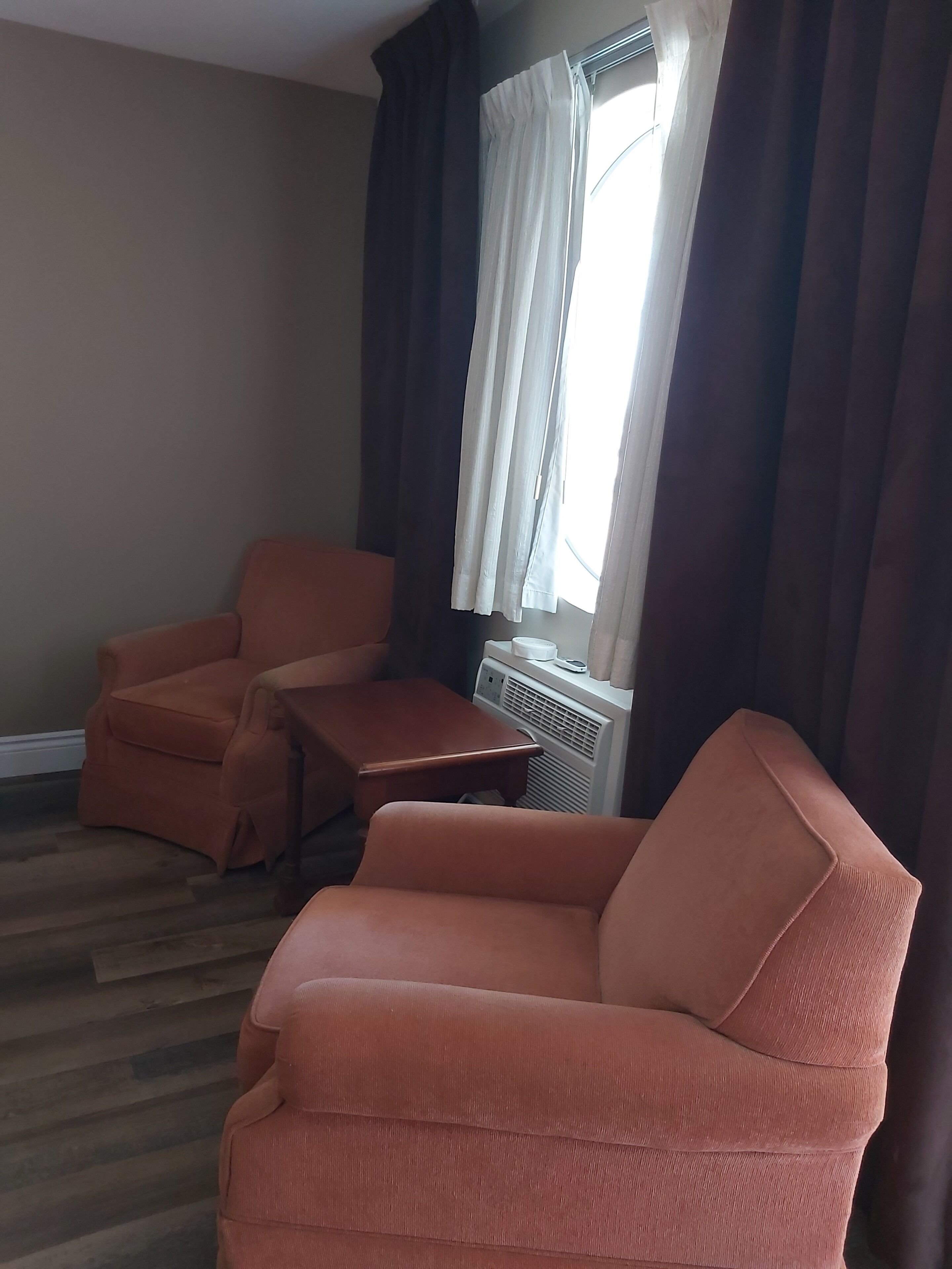 Ein Wohnzimmer mit zwei orangefarbenen Sesseln, einem kleinen Holztisch und einem Fenster mit dunklen Vorhängen.