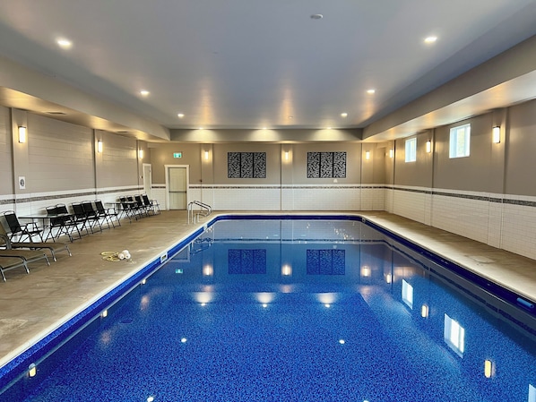 Una piscina con plataforma de azulejos, sillas de descanso y luces fijadas en la pared.