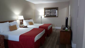 A hotel room with two beds, a desk with a computer, a TV, and a framed picture on the wall.