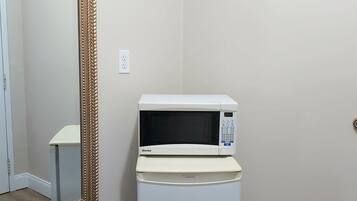 Un microondas blanco compacto sobre un pedestal blanco en una esquina, con un espejo grande y decorativo en la pared.