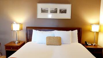 A neatly made bed with white linens and a red blanket, flanked by two bedside tables with lamps, a framed picture above the bed, and a wooden headboard.