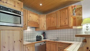 A compact kitchen with wooden cabinets, a built-in oven, a dishwasher, and a tiled backsplash.