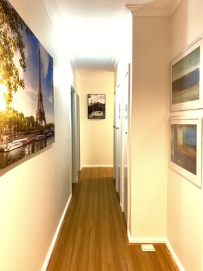 A hallway with wooden flooring, white walls, and framed pictures including the Eiffel Tower and a van. - Family Home in Prime Location (Ferntree Gully)