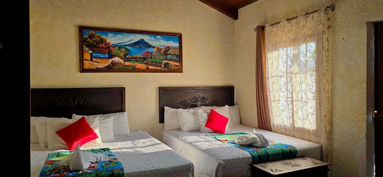 Une chambre d’hôtel avec deux lits, chacun doté d’une tête de lit, de draps blancs et d’une couverture colorée. Un tableau représentant un paysage est accroché au mur au-dessus des lits.