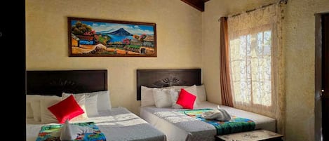 Une chambre d’hôtel avec deux lits, chacun doté d’une tête de lit, de draps blancs et d’une couverture colorée. Un tableau représentant un paysage est accroché au mur au-dessus des lits.