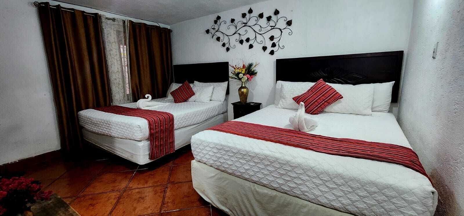 Two beds with white bedding and red accents, a decorative wall piece, and a vase with flowers.