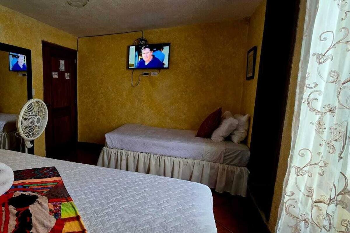 A hotel room with two beds, a television on the wall, a fan, and a towel on the bed.