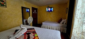 Ein Hotelzimmer mit zwei Betten, einem Fernseher an der Wand, einem Ventilator und einem Handtuch auf dem Bett.